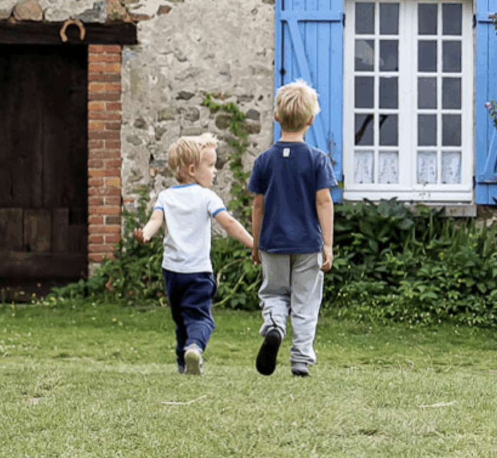 Two kids holding hands and walking through a field at a vacation rental home.