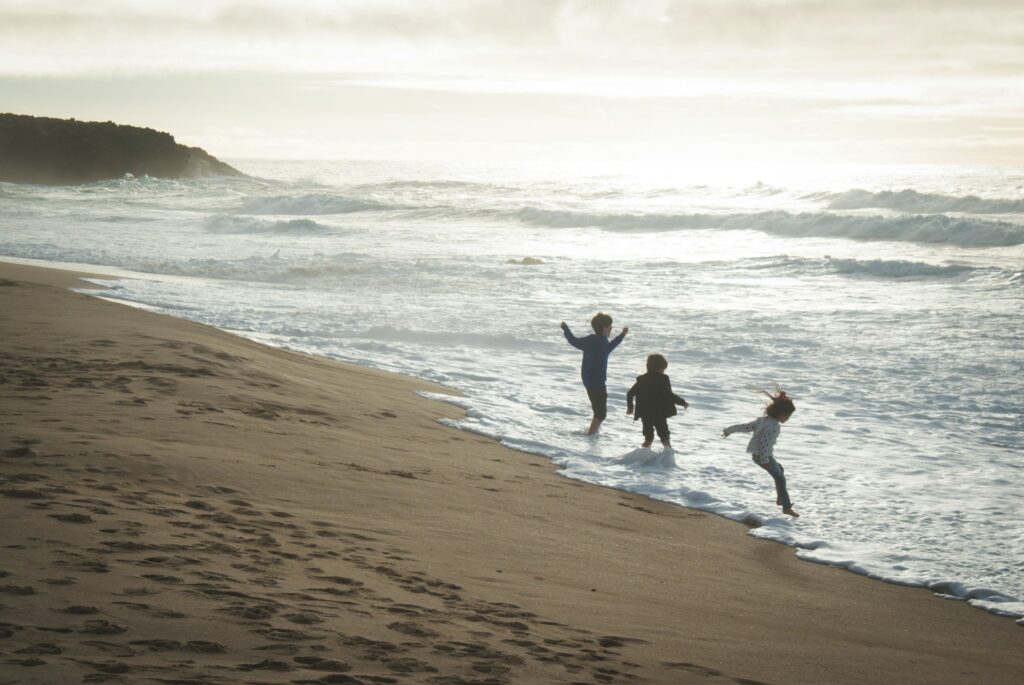Three kids playing on a beach in the waves.