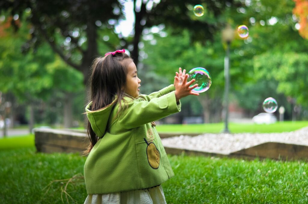 A little girl chasing bubbles in a park.
